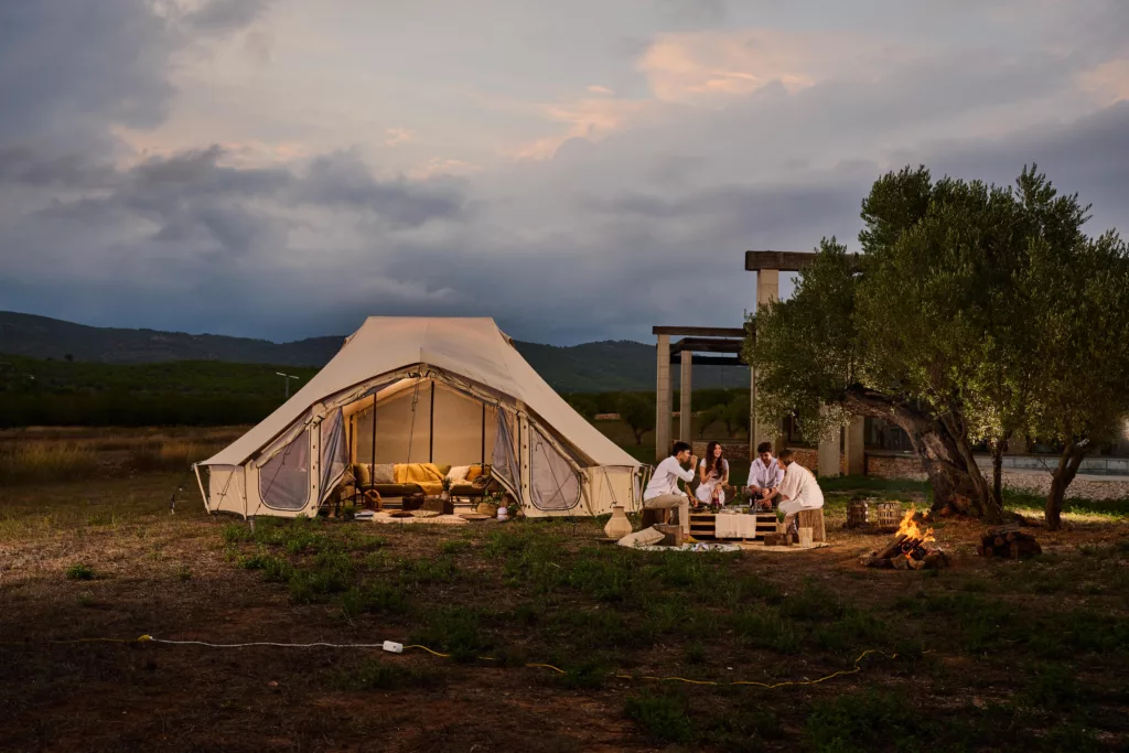 A glamping tent set up in nature at sunset with cozy outdoor seating, showcasing sustainable, boutique outdoor accommodation similar to the authentic World Tents style used at Boavida Tribe for entrepreneurial families.