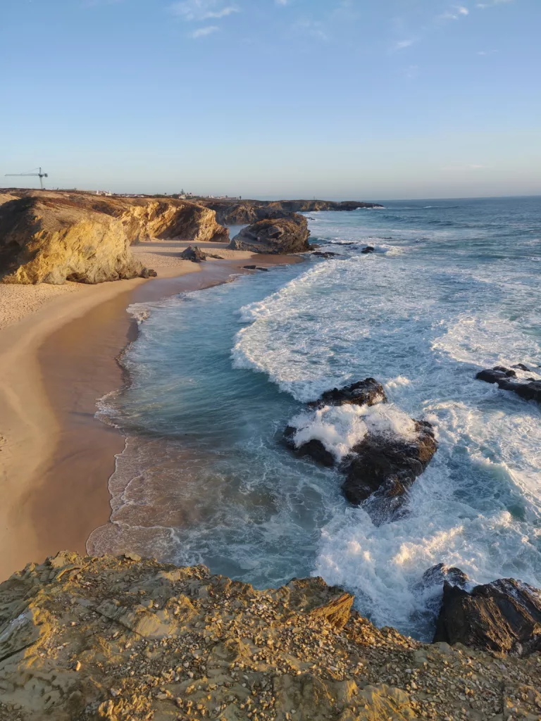 A cliffside view of the Portuguese west coast with waves crashing against rocky formations, showcasing the natural beauty of Portugal’s wild, undeveloped beaches.